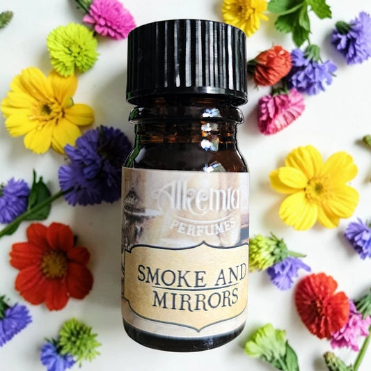 A small amber glass perfume bottle with a black ribbed cap and a cream label reading 'Alkemia Perfumes' and 'Smoke and Mirrors,' photographed from above on a white surface surrounded by colorful flowers.
Alkemia Smoke and Mirrors fragrance samples UK 1ml sample available 