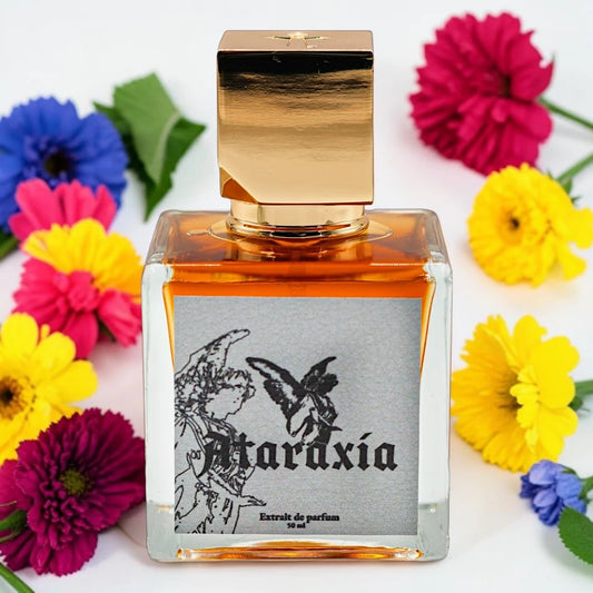 A square glass perfume bottle filled with amber liquid, topped with a reflective metallic gold cap, and surrounded by colorful artificial flowers on a white background. The front label reads 'Ataraxia' with black line art of a winged figure and butterfly. Ataraxia Amaretto Jazz In The Melting Room | Fragrance Sample UK 1ml 2ml 5ml perfume samples