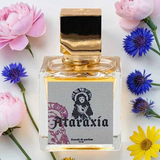 A square glass perfume bottle with a metallic gold cap and a gray label reading 'Ataraxía Extrait de parfum 50 ml', surrounded by pink and blue flowers on a white background. Ataraxia My Doll's Makeup| Fragrance Sample UK