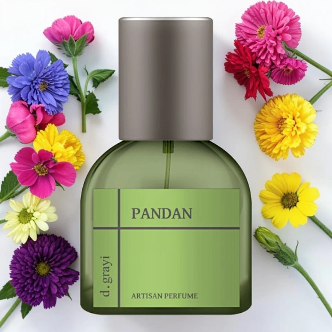 A bottle of d. grayi PANDAN artisan perfume with a green body and metallic silver cap, surrounded by colorful flowers on a white background.