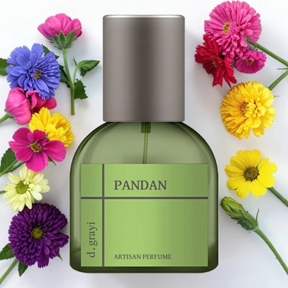 A bottle of d. grayi PANDAN artisan perfume with a green body and metallic silver cap, surrounded by colorful flowers on a white background.