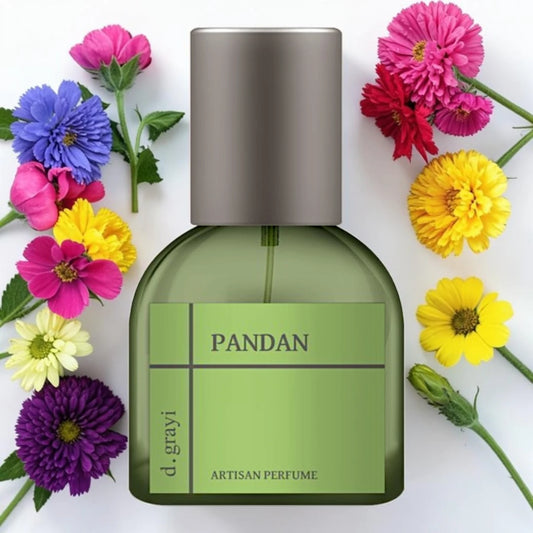 A bottle of d. grayi PANDAN artisan perfume with a green body and metallic silver cap, surrounded by colorful flowers on a white background.