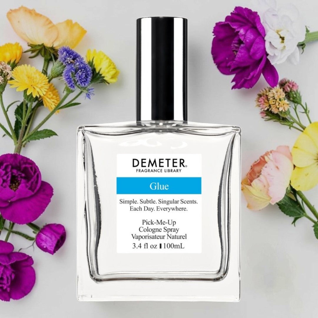 A bottle of Demeter Fragrance Library Glue cologne spray, surrounded by colorful flowers on a light gray background. Demeter Fragrance Library Glue | Fragrance Samples UK 1ml 2ml and 5ml perfume samples available 