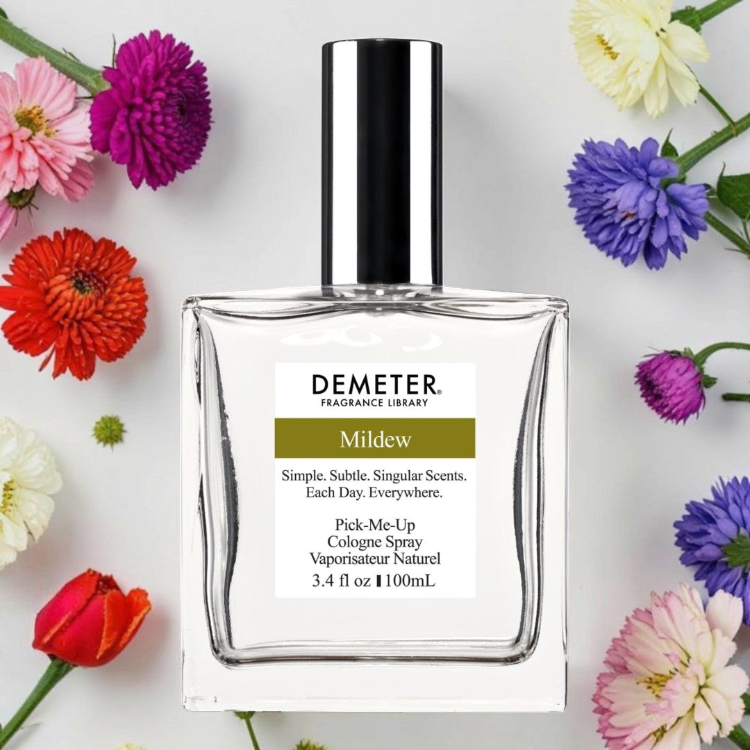 A bottle of Demeter Fragrance Library 'Mildew' cologne spray, surrounded by colorful flowers on a light gray background. Demeter Fragrance Library Mildew | Fragrance Samples UK 1ml 2ml and 5ml perfume samples available 