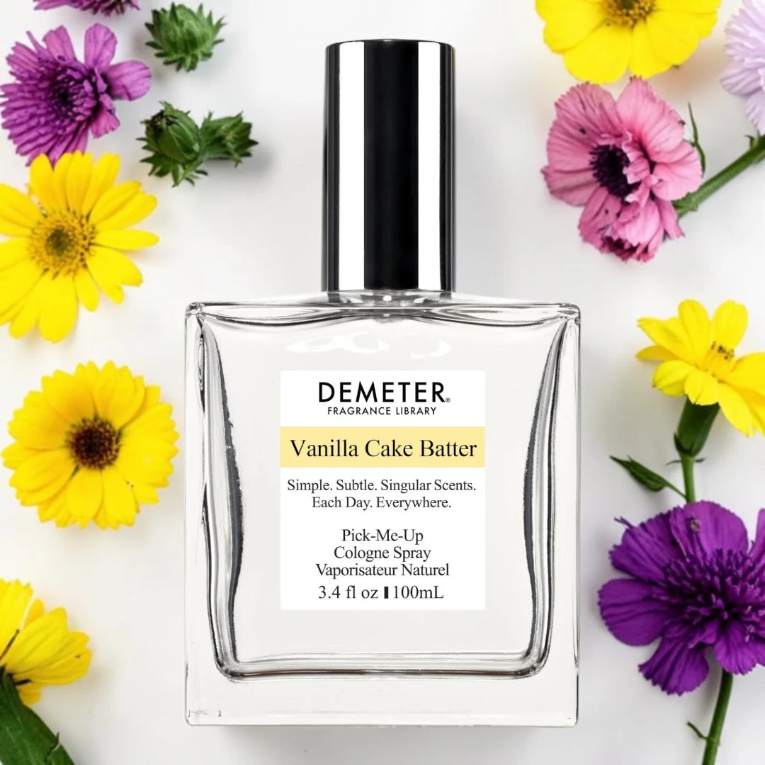 A bottle of Demeter Vanilla Cake Batter cologne spray, surrounded by colorful yellow, pink, and purple flowers on a white background.