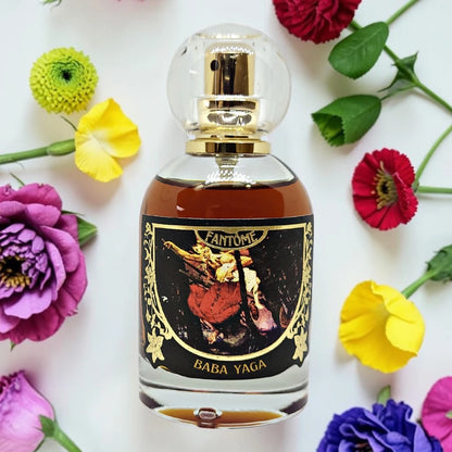 A glass perfume bottle with a clear spherical cap and gold spray mechanism, filled with amber liquid. The bottle has a black label with gold detailing and an illustration, labeled 'FANTOME' and 'BABA YAGA'. available