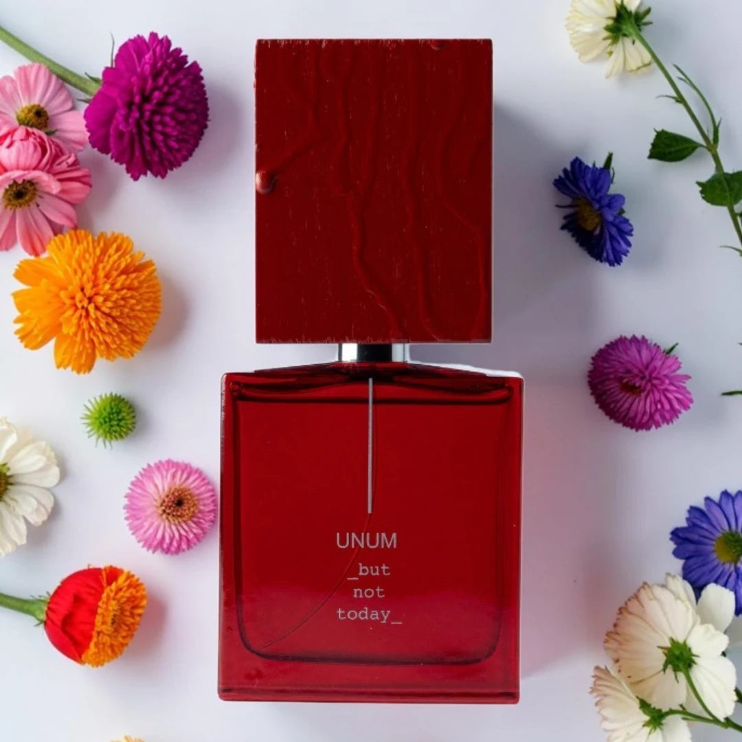 A red rectangular perfume bottle labeled 'UNUM but not today' sits centered on a white background, surrounded by colorful flowers in pink, orange, purple, blue, and white. Filippo Sorcinelli But Not Today | Fragrance Samples UK