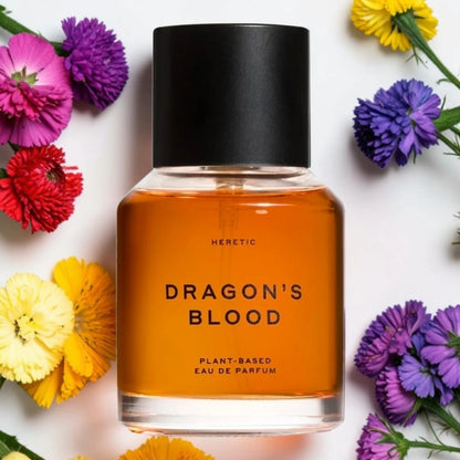 A bottle of Heretic Dragon's Blood Eau De Parfum with amber liquid and a black cap, surrounded by colorful flowers on a white background. Heretic Dragon's Blood Fragrance Samples UK 1ml 2ml and 5ml perfume samples available 
