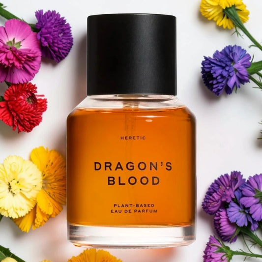 A bottle of Heretic Dragon's Blood Eau De Parfum with amber liquid and a black cap, surrounded by colorful flowers on a white background. Heretic Dragon's Blood Fragrance Samples UK 1ml 2ml and 5ml perfume samples available 