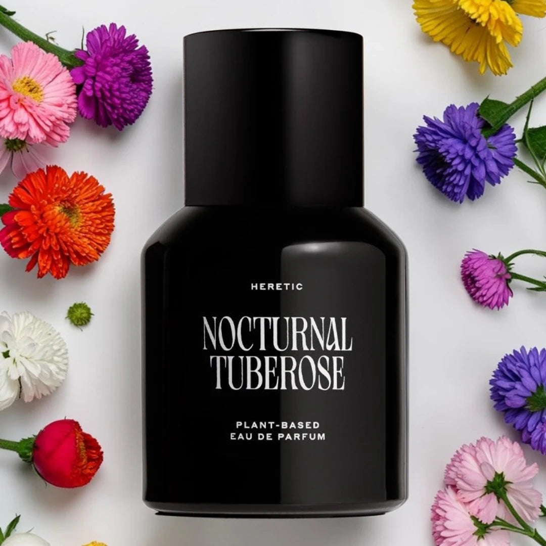 A matte black perfume bottle labeled 'HERETIC NOCTURNAL TUBEROSE PLANT-BASED EAU DE PARFUM' centered on a white background, surrounded by colorful flowers including pink, purple, red, orange, yellow, and white.
Heretic Nocturnal Tuberose | Fragrance Samples UK