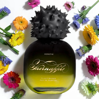 A bottle of Heretic Shonafille plant-based eau de parfum with a black spiky cap and a yellow-to-black gradient bottle, surrounded by colorful daisy flowers on a white background. Heretic Thornapple Fragrance Samples UK 1ml 2ml and 5ml perfume samples available 