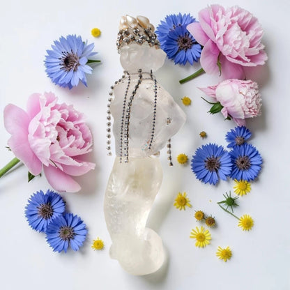 A translucent white crystal mermaid figurine adorned with a pearl crown and silver beaded necklaces, styled in a flat lay with pink peonies, blue cornflowers, and small yellow wildflowers on a white background. House Of Atropa Mermaids Steal Ice Cream | Fragrance Samples UK 1ml 2ml and 5ml perfume samples available 