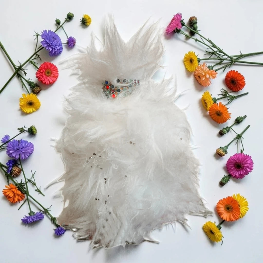 A white feather boa or decorative feather accessory laid flat on a white background, surrounded by colorful flowers including purple, pink, orange, yellow, and red. House Of Atropa She Is Cat | Fragrance Samples UK 1ml 2ml and 5ml perfume samples available 