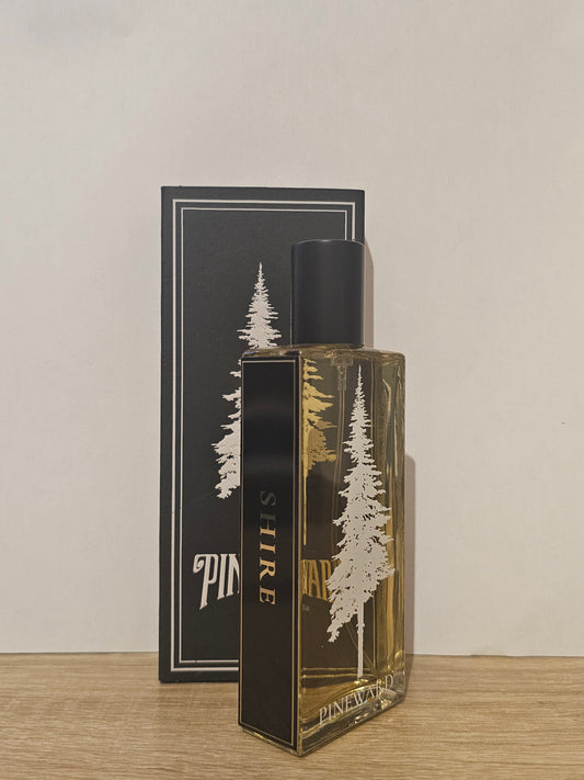 A rectangular glass perfume bottle with amber liquid and a black cap, standing in front of its black packaging box. The bottle and box feature a white pine tree illustration and the brand name 'SHIRE'. Pineward Shire | Fragrance Samples UK 1ml 2ml and 5ml perfume samples available 