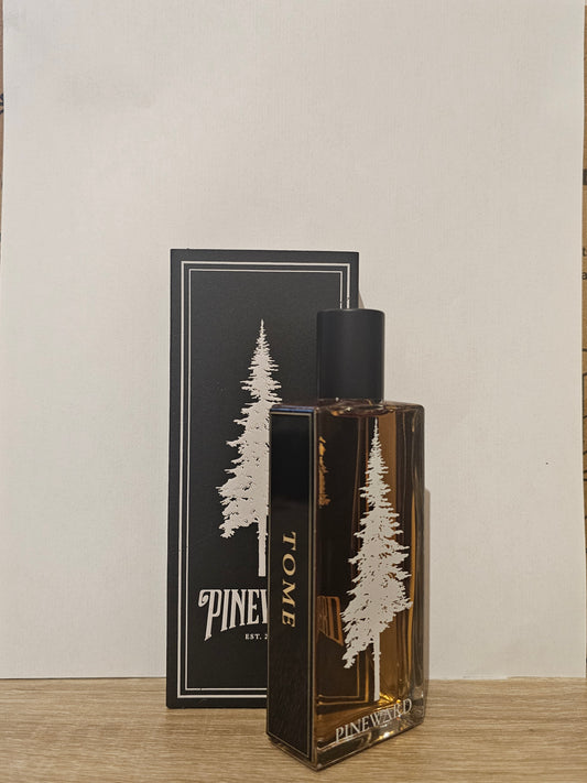 Pine Valley TOME fragrance bottle with amber liquid and a black cap, standing in front of its black packaging box with white pine tree illustrations on a light wood surface. Pineward Tome | Fragrance Samples UK 1ml 2ml and 5ml perfume samples available 