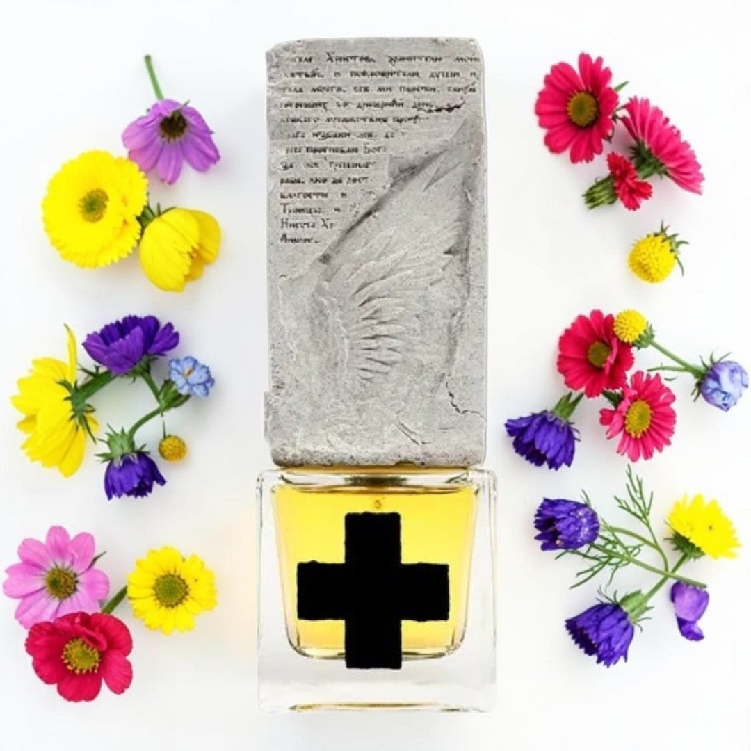 A rectangular perfume bottle with a clear glass base showing yellow liquid and a bold black cross on the front, topped with a textured gray stone-like cap featuring an embossed wing and script. The bottle is centered on a white background and surrounded by colorful daisy flowers in pink, yellow, and purple. Profundum + | Fragrance Sample UK 1ml 2ml and 5ml perfume samples available 