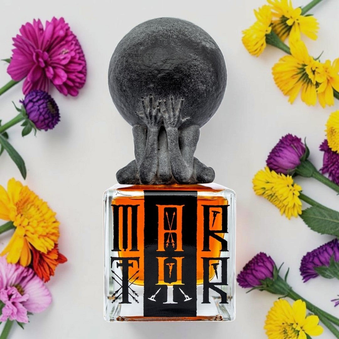 A perfume bottle with a sculptural black figure holding a large sphere on its head, surrounded by colorful flowers on a white background. The bottle label features the word 'MARIA' in stylized black and orange lettering. Profundum Martyr | Fragrance Sample UK 1ml 2ml and 5ml perfume samples available