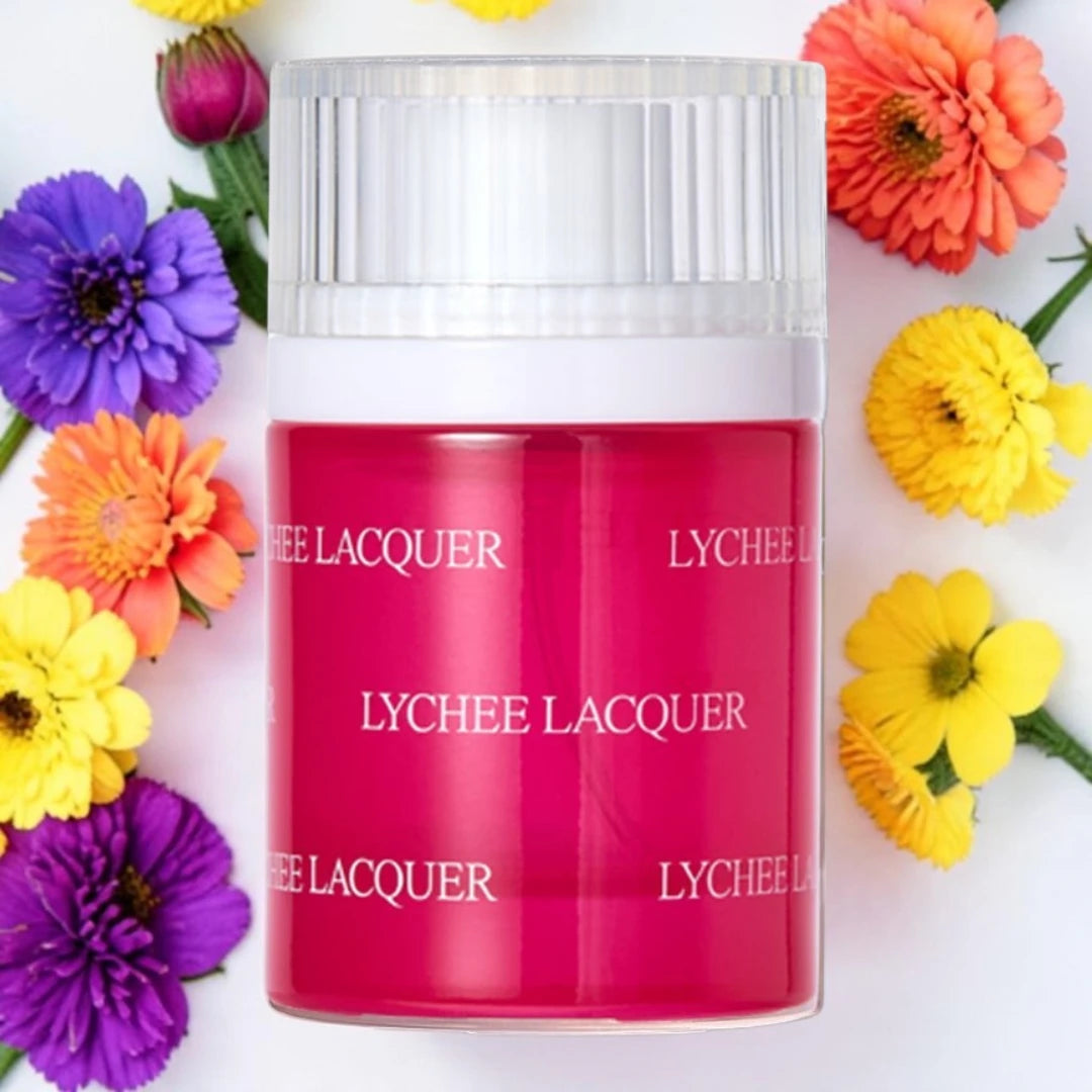 A jar of Lychee Lacquer cosmetic product with a translucent cap and a bright pink-red body, surrounded by colorful flowers on a white background.