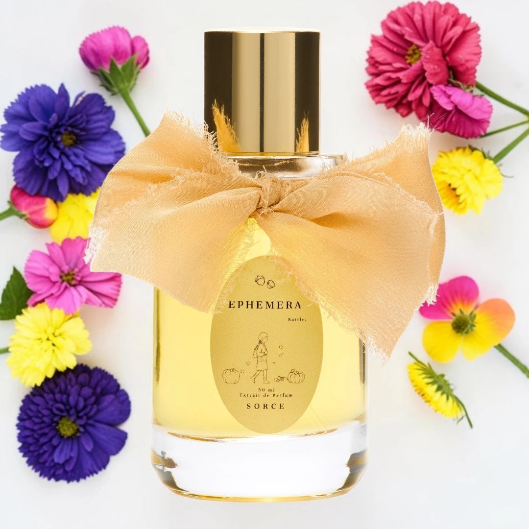 A clear glass perfume bottle filled with pale yellow liquid, topped with a reflective gold cap and wrapped with a large peach satin bow. The front label reads Ephemera and Sorce.
Sorce Ephemera | Fragrance Samples UK available in 1ml 2ml 5ml 10ml