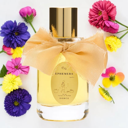 A clear glass perfume bottle filled with pale yellow liquid, topped with a reflective gold cap and wrapped with a large peach satin bow. The front label reads Ephemera and Sorce.
Sorce Ephemera | Fragrance Samples UK available in 1ml 2ml 5ml 10ml