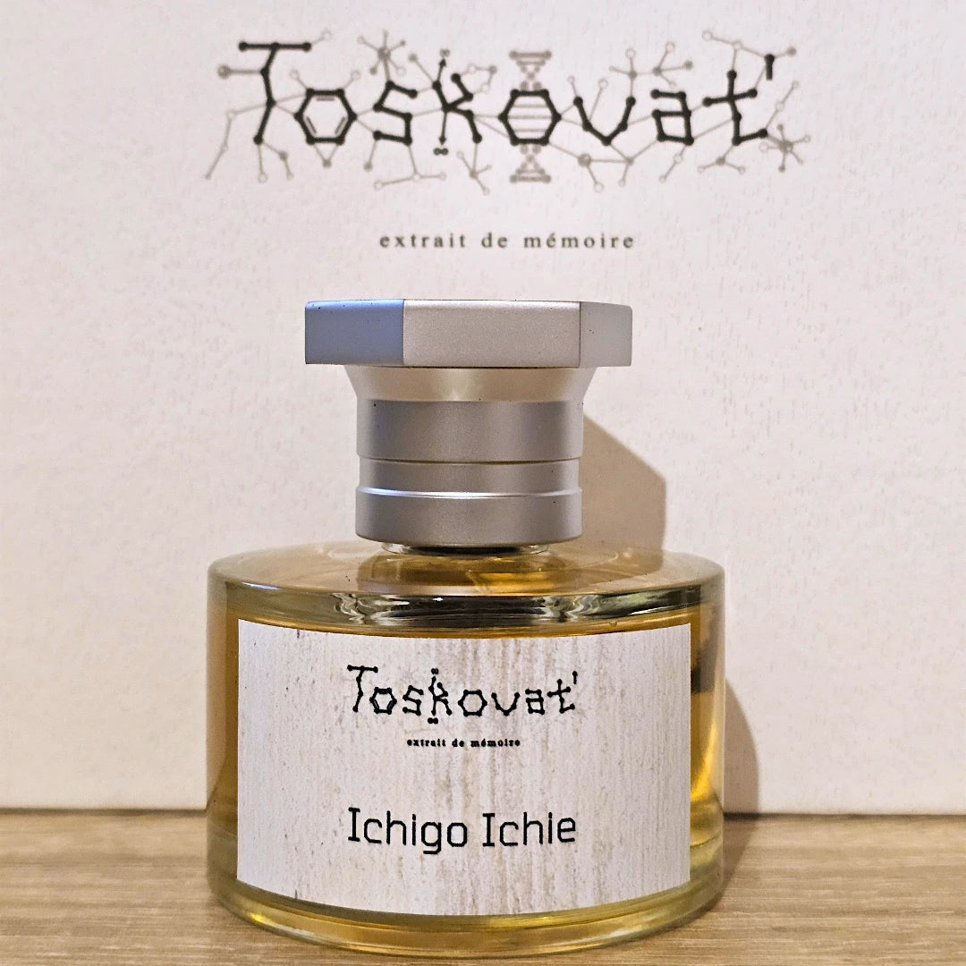 A bottle of Toskovat 'Ichigo Ichle' extrait de mémoire perfume, featuring a clear glass bottle with golden-amber liquid, a textured off-white label, and a metallic silver cap, set against its branded beige background.