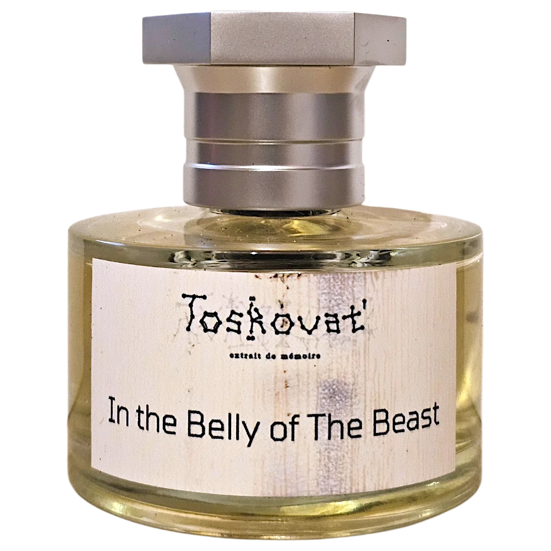 A bottle of Toskóvat 'In the Belly of The Beast' eau de mémoire perfume, featuring a clear glass bottle with pale yellow liquid, a white textured label, and a silver-toned metal cap, isolated on a white background.
