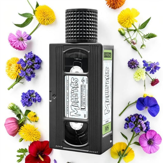 A novelty black VHS-shaped bottle or container with a textured top, surrounded by colorful flowers on a white background. The front label reads 'Maltins' and the side label shows 'VHS' and 'Maltins'.