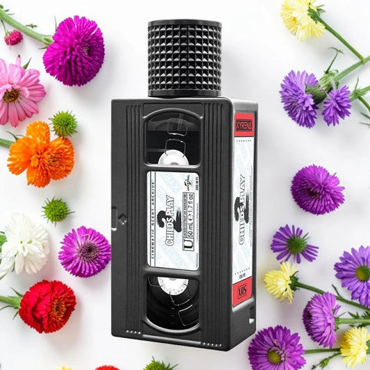 A novelty VHS-shaped bottle or container with a black textured cap and retro tape label, photographed from above on a white background and surrounded by colorful flowers.
Xyrena child's play 2| Fragrance Samples UK 1ml 2ml and 5ml perfume samples available 